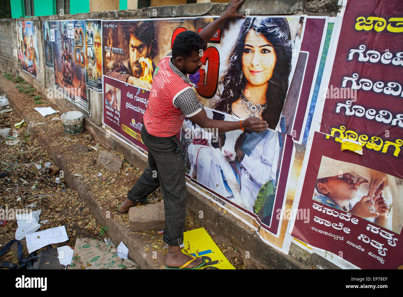 Man sticks Bollywood film posters to a wall in Hassan Stock Photo