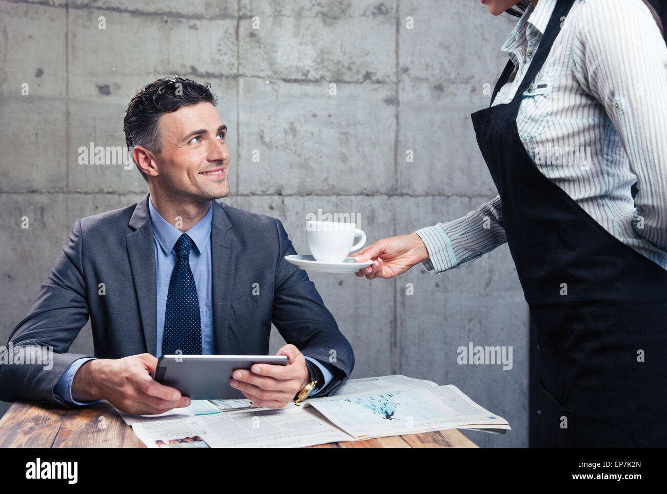 Waitress giving cup with coffee to happy man in suit at restaurant Stock Photo