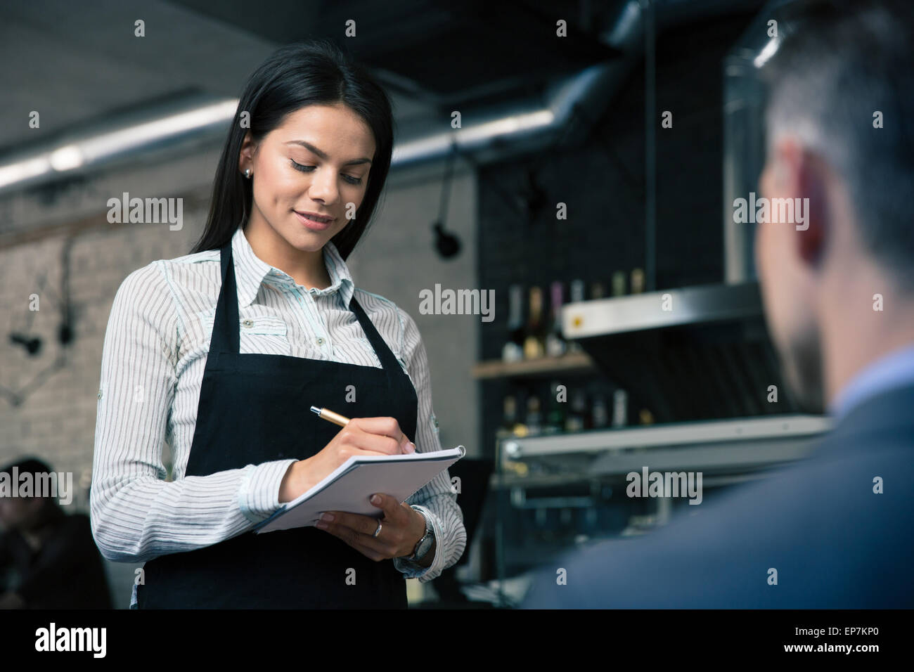 Female waiter in apron writing order in restaurant Stock Photo