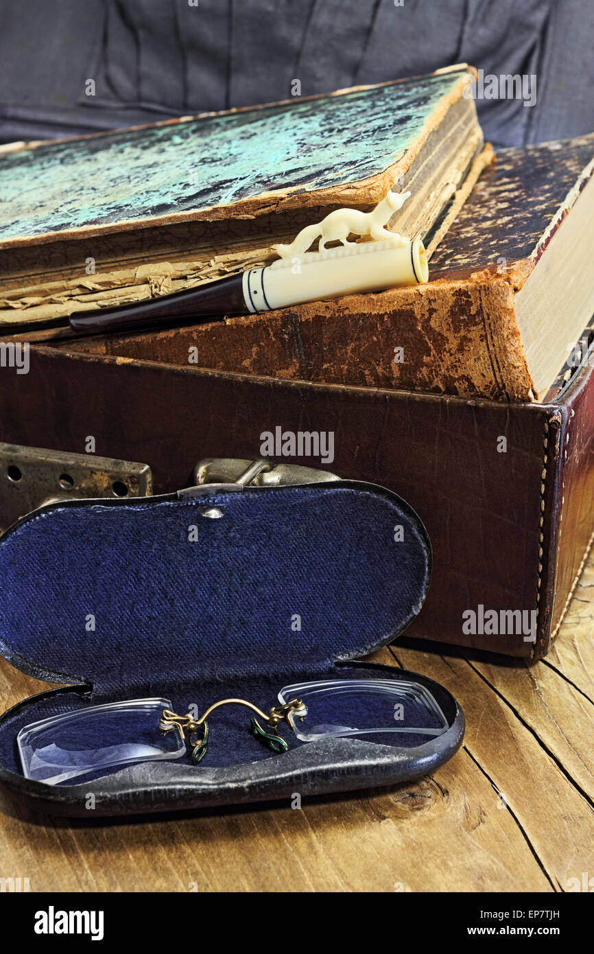 Old stuff. Leather suitcase with old books, cigarette holder with a bone carving and pince-nez in a metal box. Stock Photo