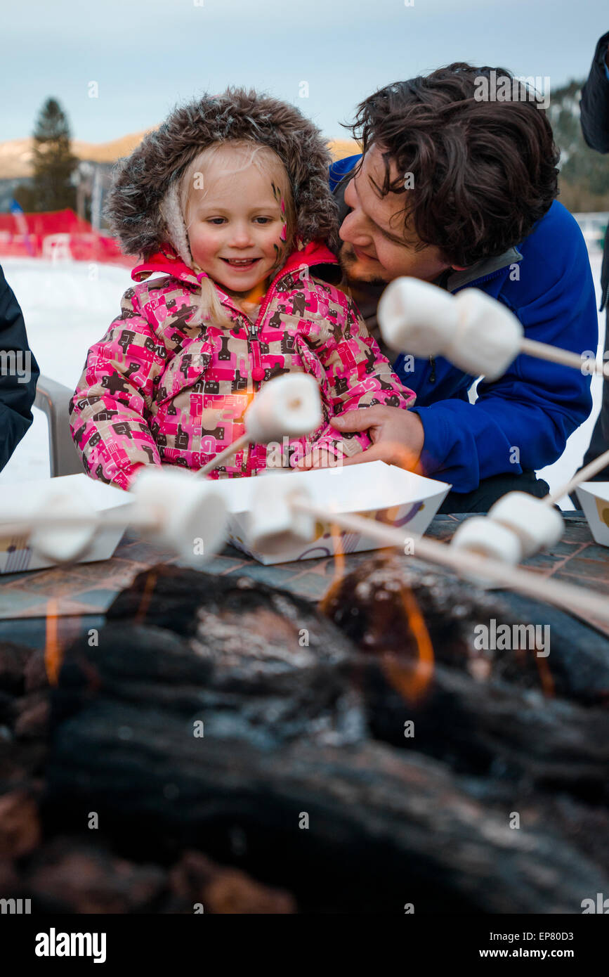 Daughter roasting marshmellows with father over fire in the snow at