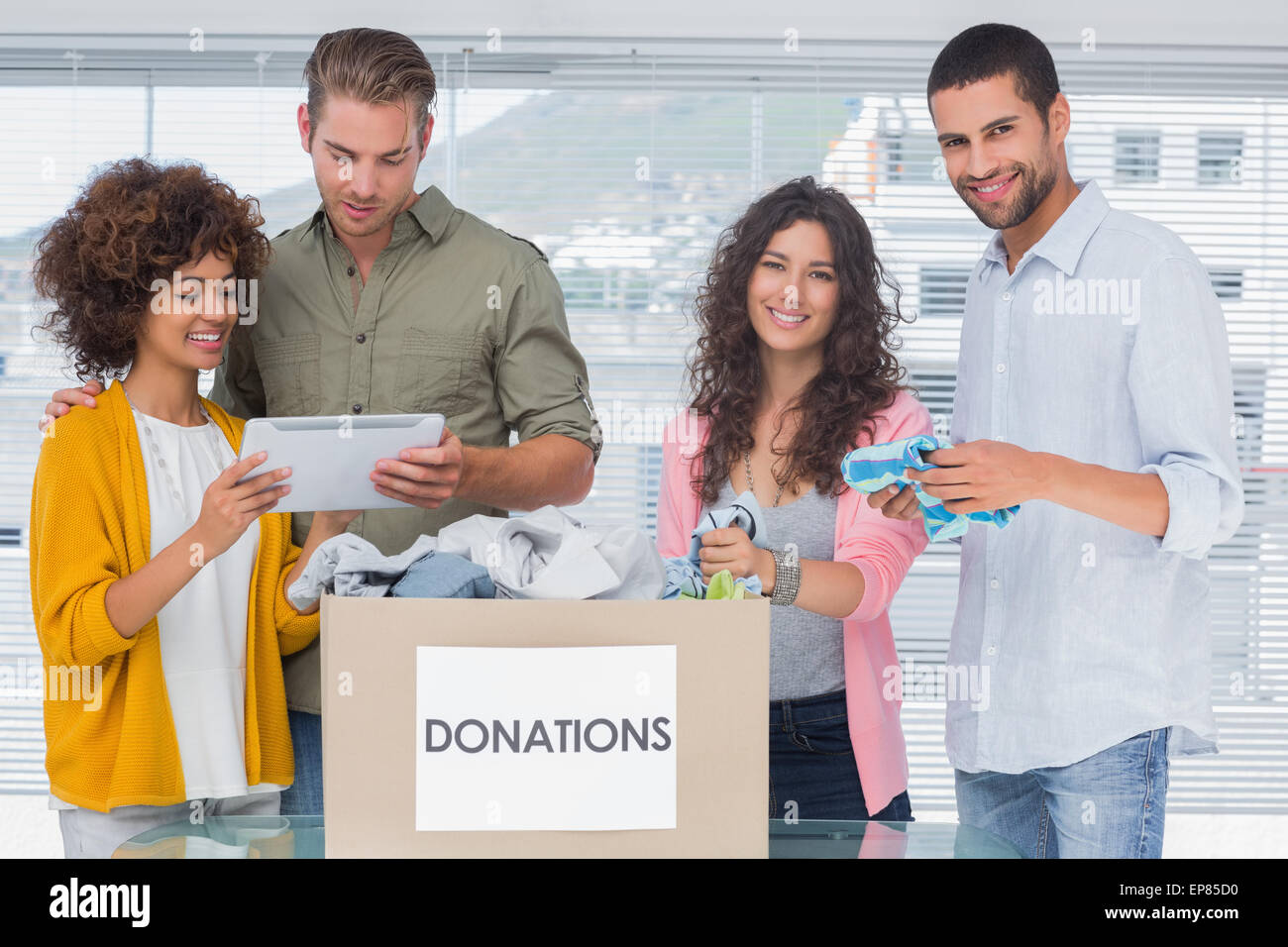 Smiling volunteers using tablet and taking out clothes from donations Stock Photo