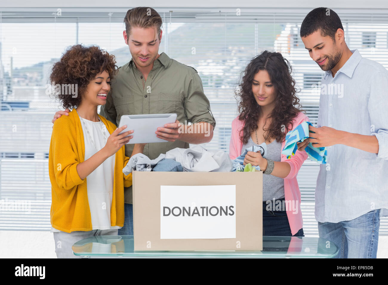 Volunteers using tablet and taking out clothes from a donation box Stock Photo