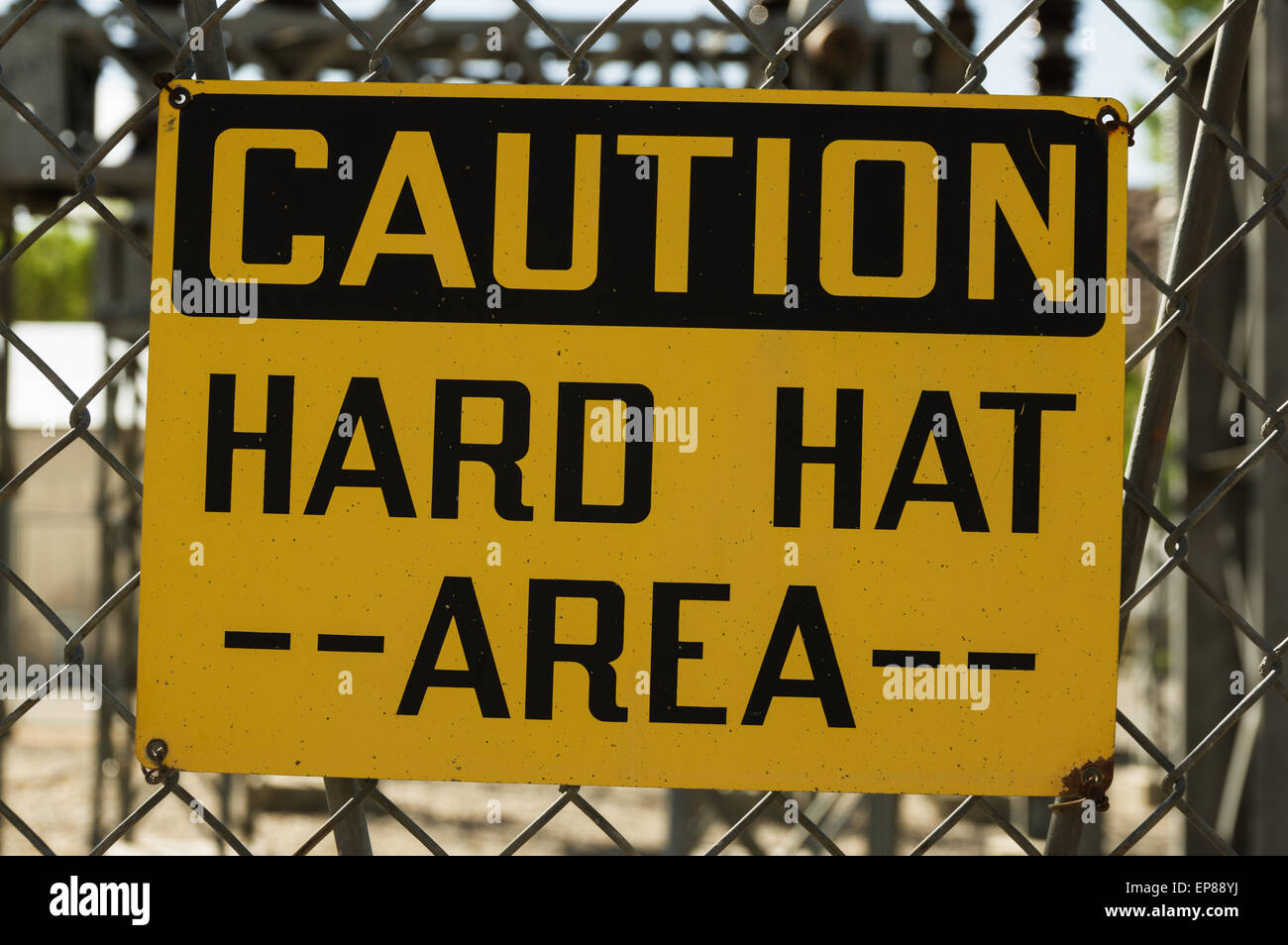 yellow and black caution hard hat area sign wired to a chain link fence Stock Photo