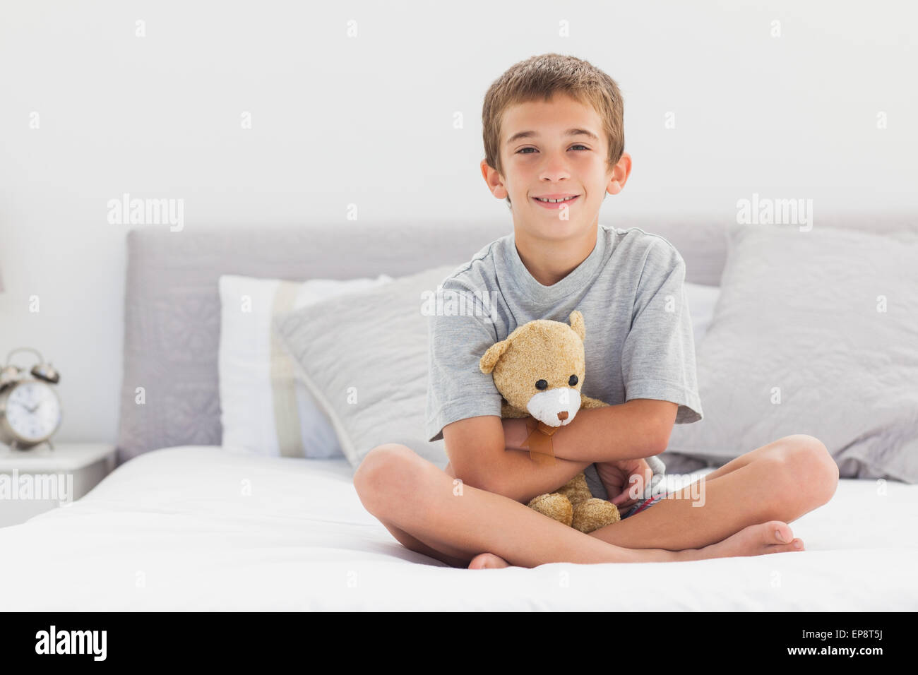 Smiling little boy sitting on bed holding his teddy bear Stock Photo ...