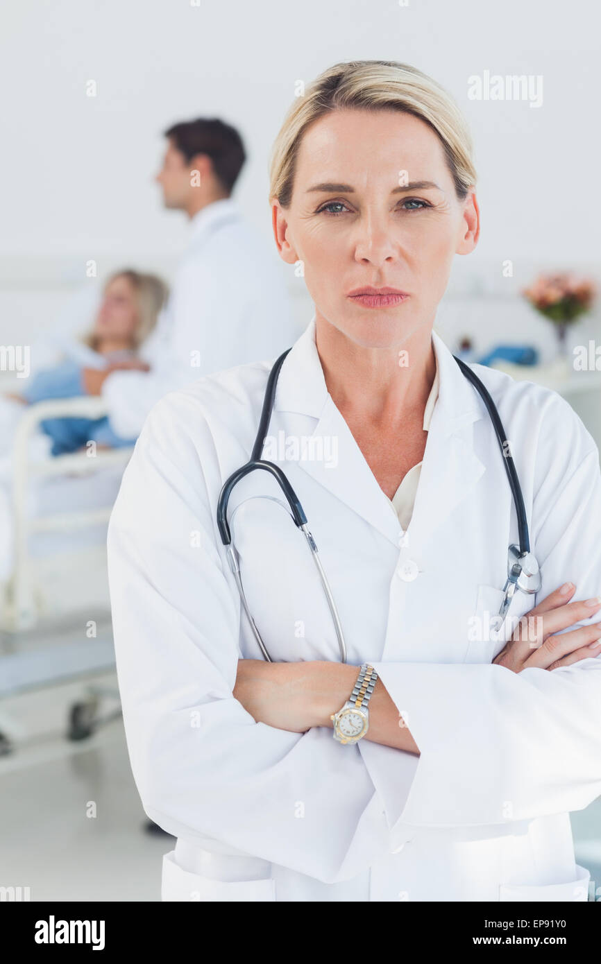 Serious doctor posing with doctor attending patient on background Stock