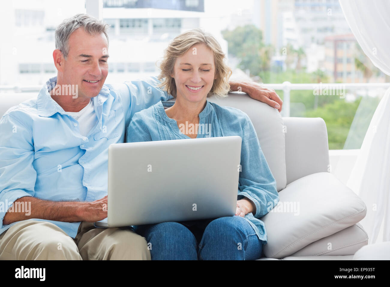 Cheerful couple relaxing on their couch using the laptop Stock Photo ...