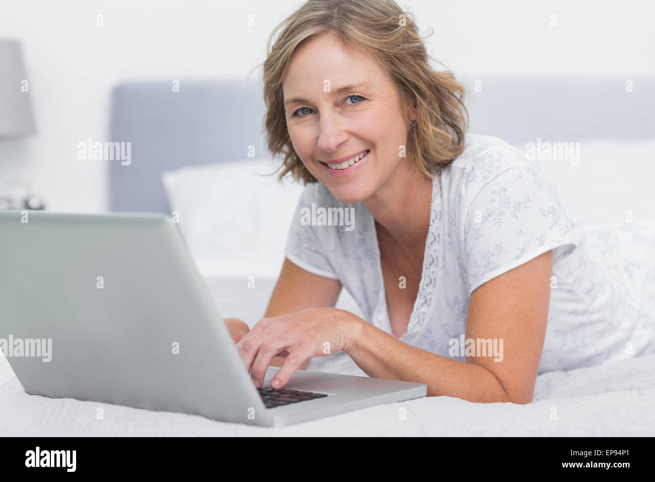 Smiling blonde woman lying on bed using laptop Stock Photo - Alamy