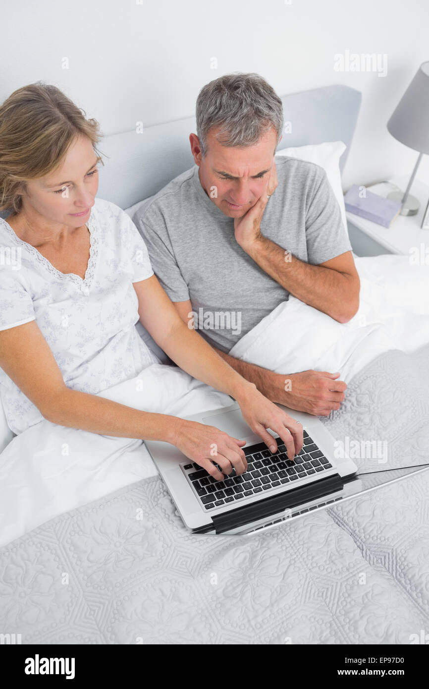 Thoughtful couple using their laptop together in bed Stock Photo - Alamy