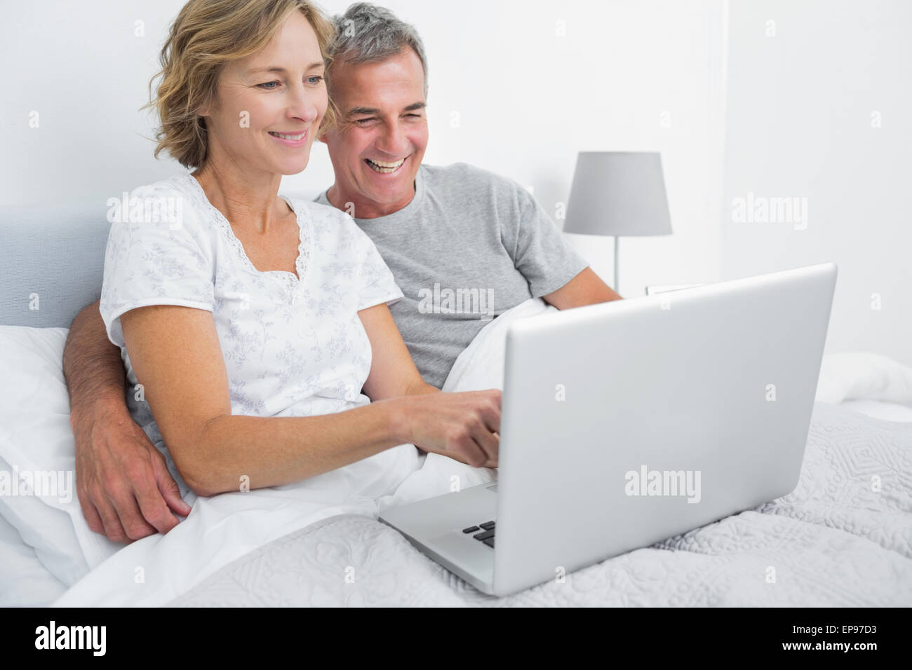 Smiling couple using their laptop together in bed Stock Photo - Alamy