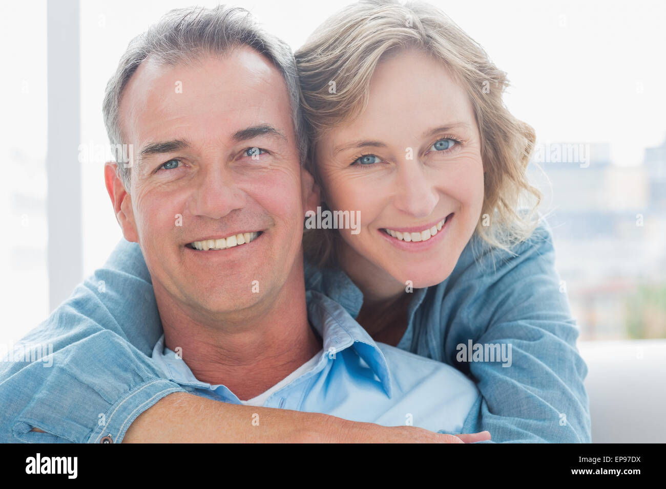 Smiling woman hugging her husband on the couch from behind Stock Photo ...
