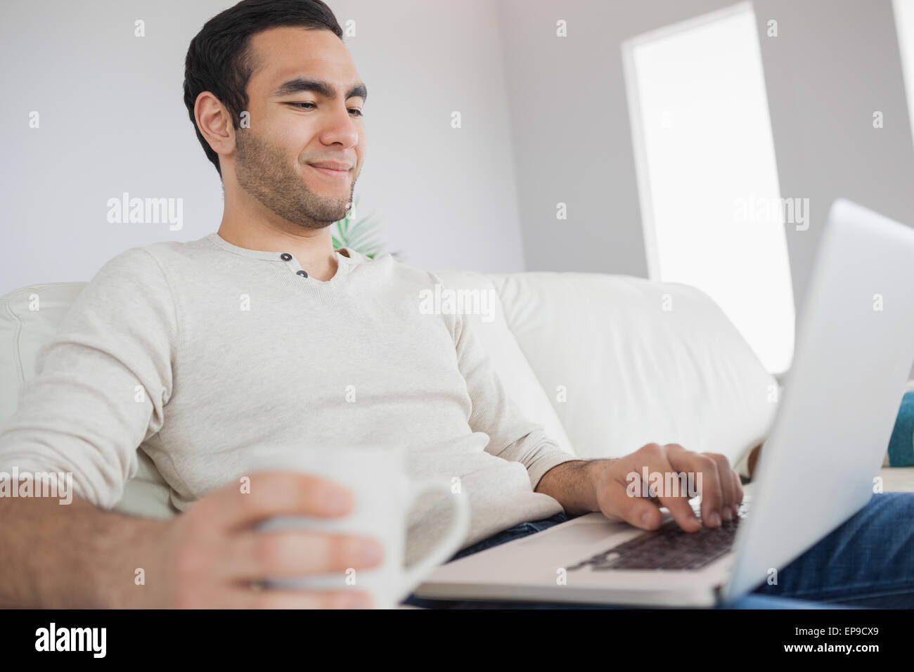 Peaceful handsome man having coffee while using his laptop Stock Photo