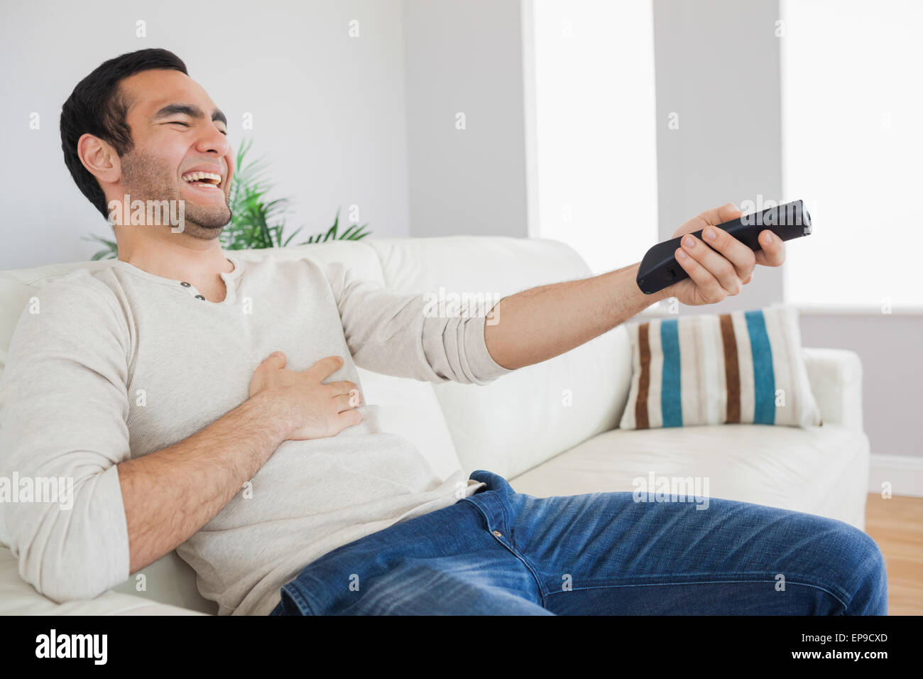 Handsome man bursting out laughing while watching tv Stock Photo Alamy