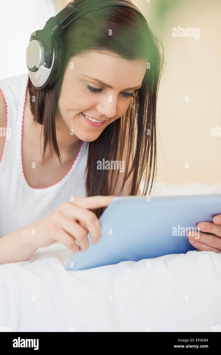 Happy girl listening to music and using a tablet pc lying on a bed Stock Photo