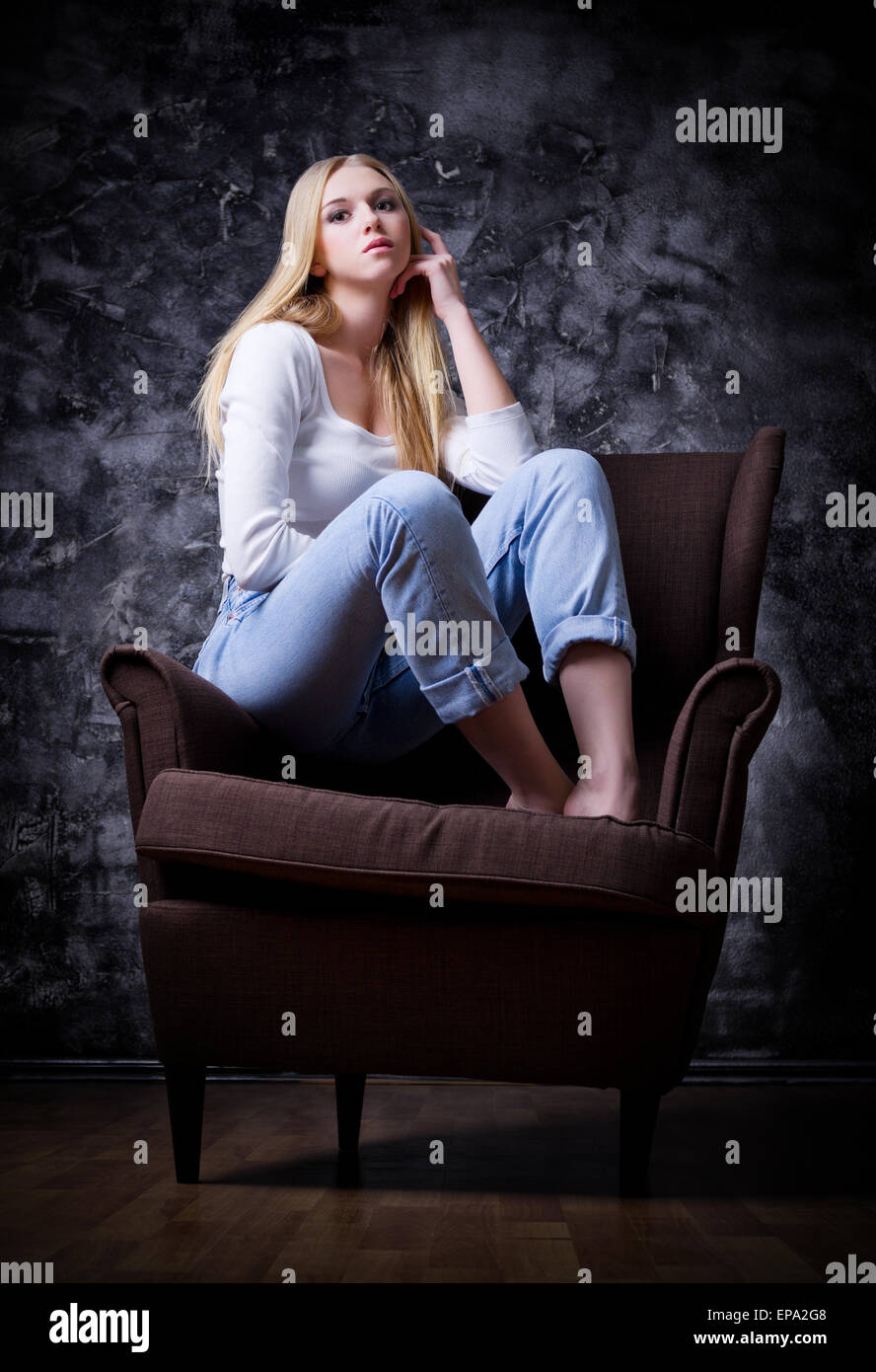 Young girl sit on the chair on grey wall background Stock Photo
