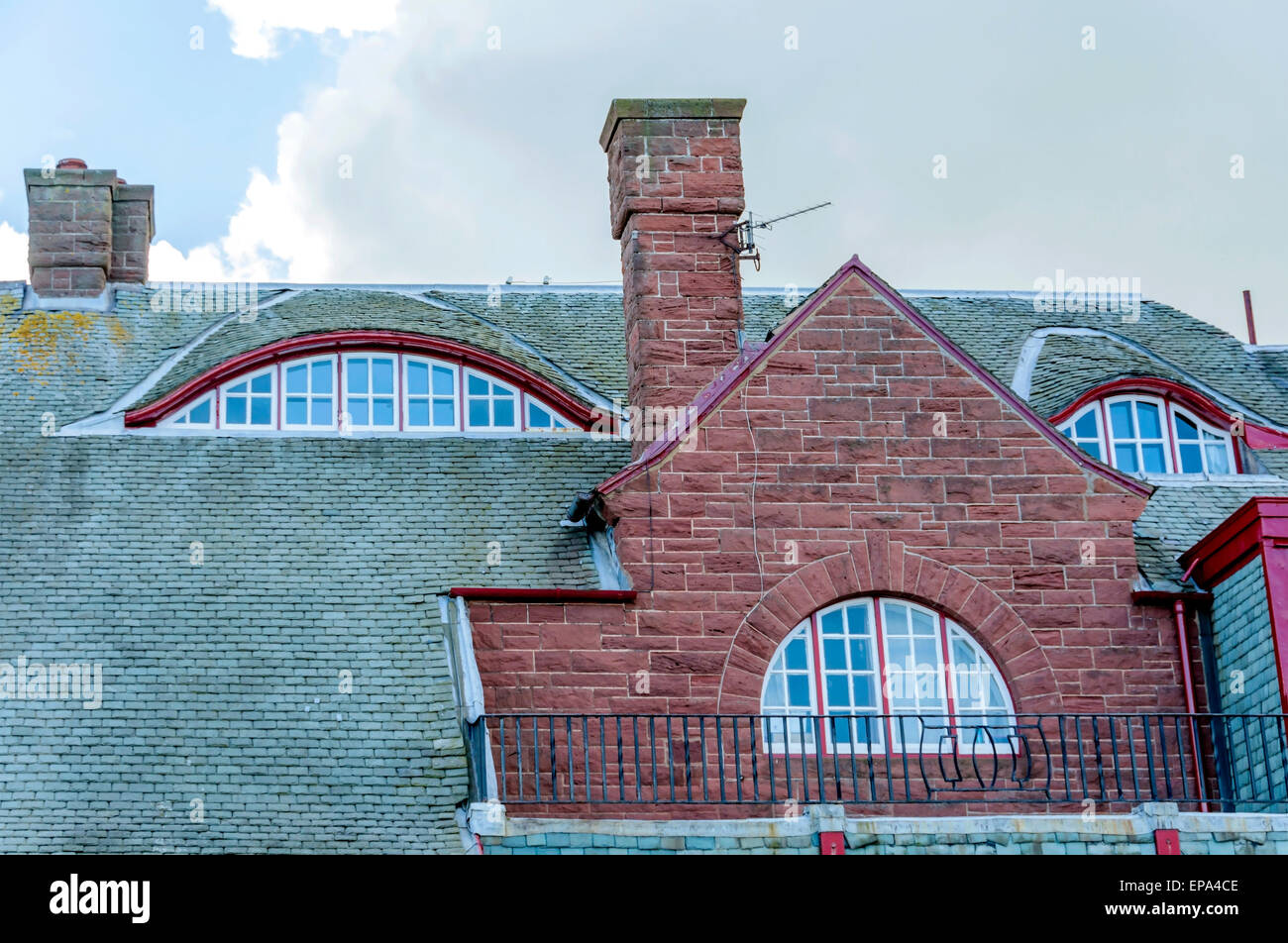 The complex roof of an Arts & Crafts house, with arched windows and curved slated roof lights and tall sandstone chimney pieces. Stock Photo