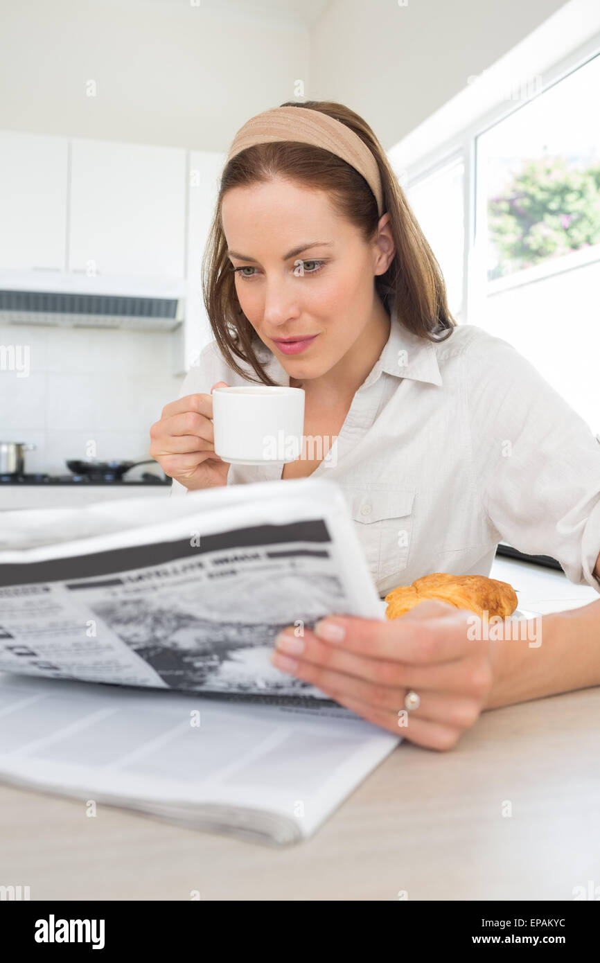 Woman with coffee cup reading newspaper in kitchen Stock Photo Alamy