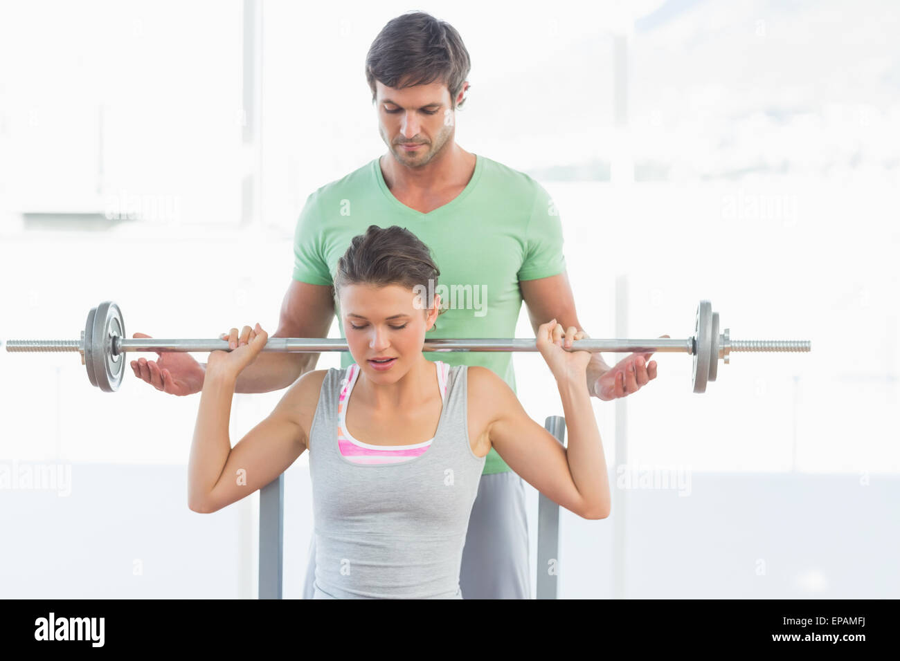 Trainer helping fit woman to lift barbell bench press Stock Photo - Alamy