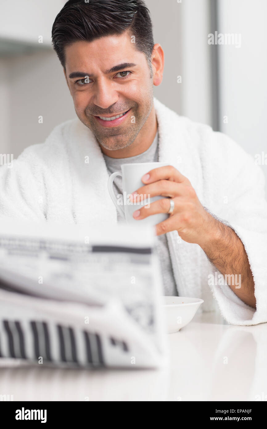 Smiling man with coffee cup reading newspaper in kitchen Stock Photo