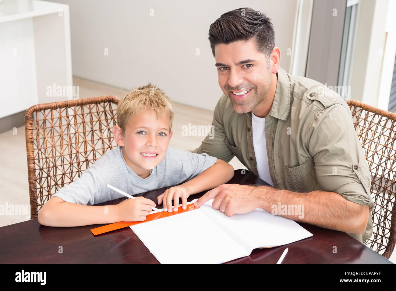 Smiling father helping son with homework at table Stock Photo - Alamy
