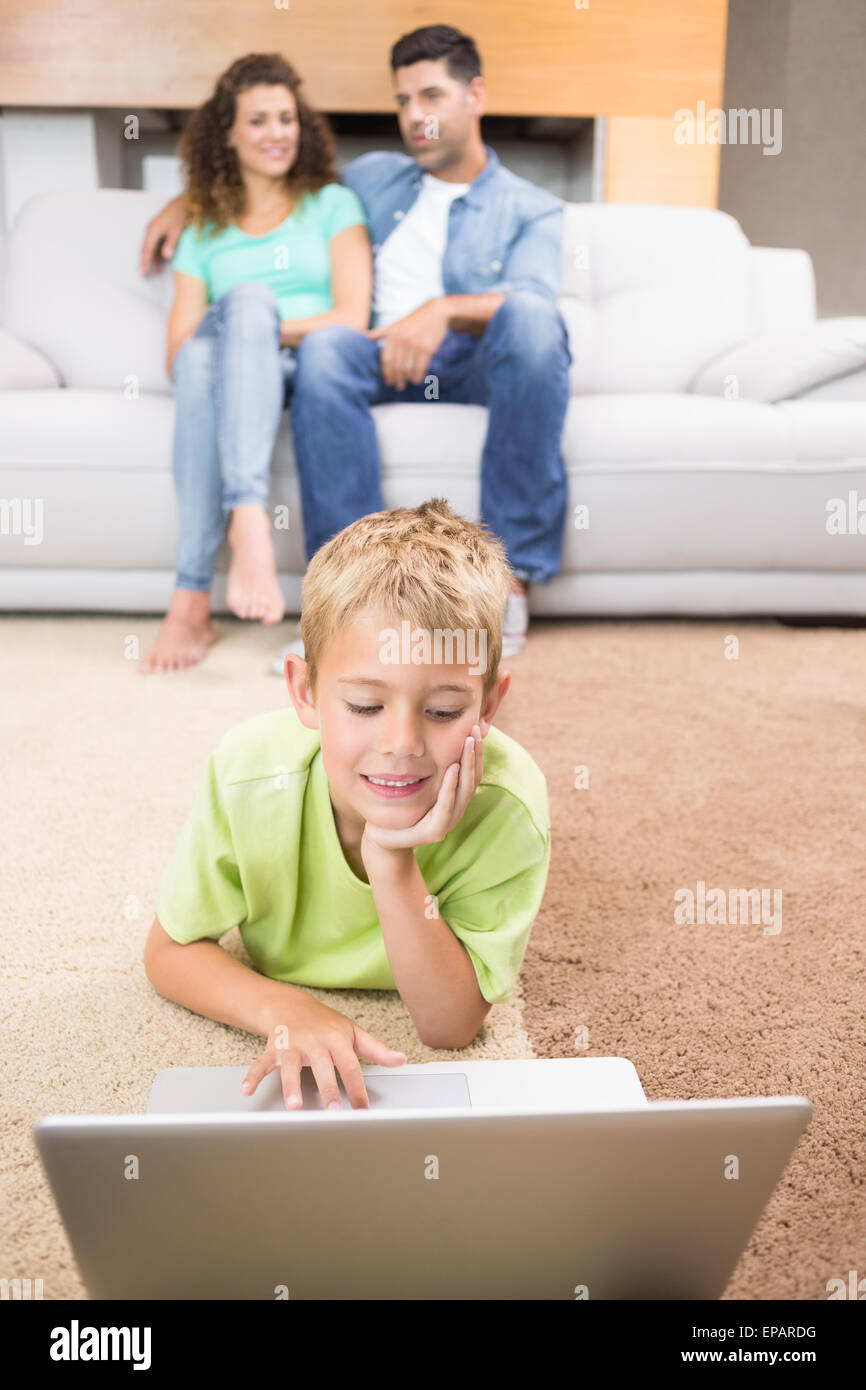Cute little boy using laptop on the rug with parents sitting sofa Stock ...
