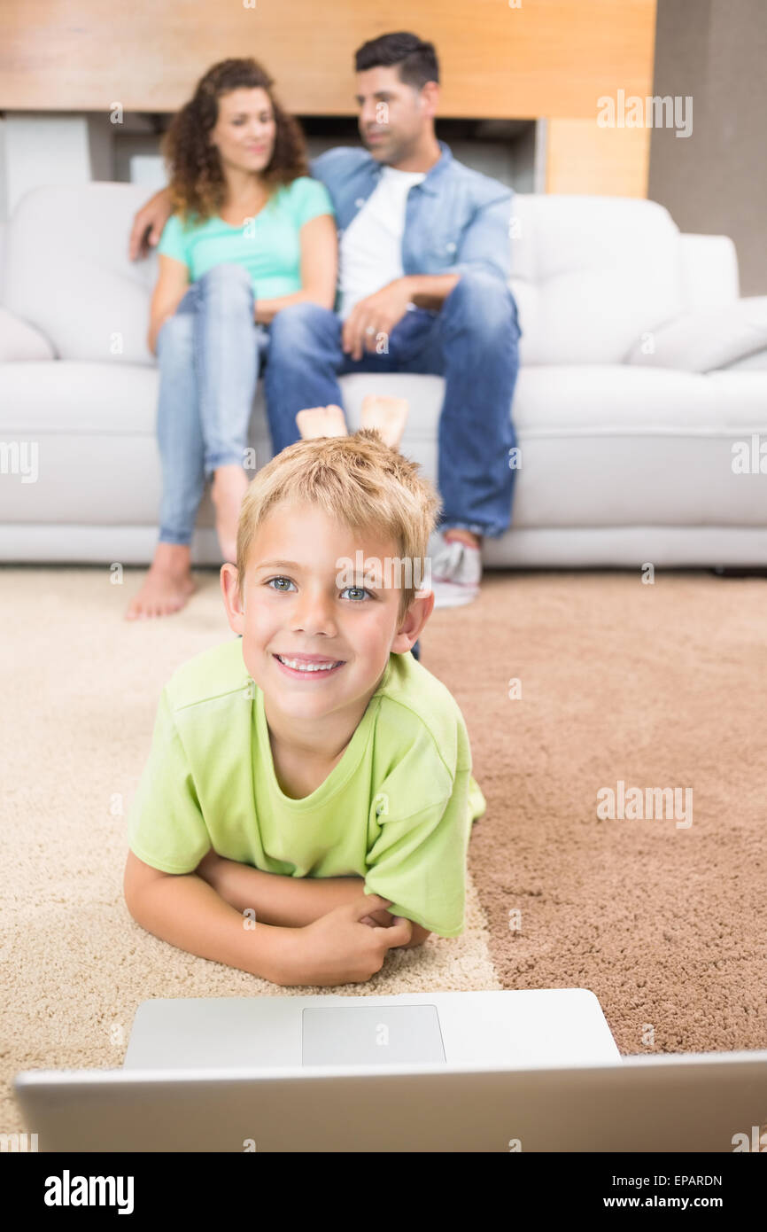 Happy little boy using laptop on the rug with parents sitting sofa ...