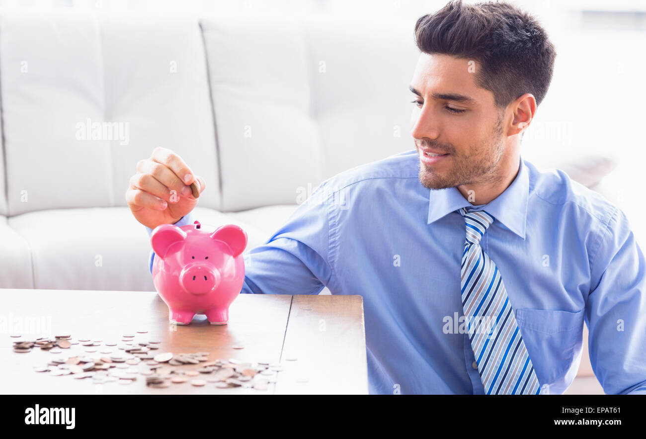 Handsome businessman putting coins into piggy bank Stock Photo - Alamy