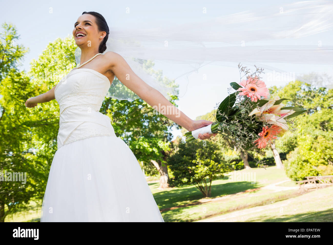 Cheerful young beautiful bride with bouquet in park Stock Photo - Alamy