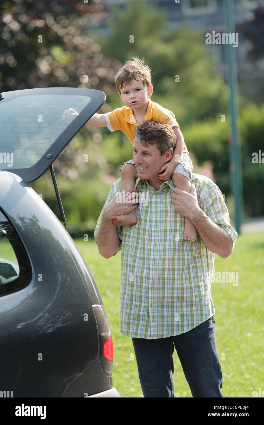 Son on Fathers shoulder standing at the back of his car Stock Photo