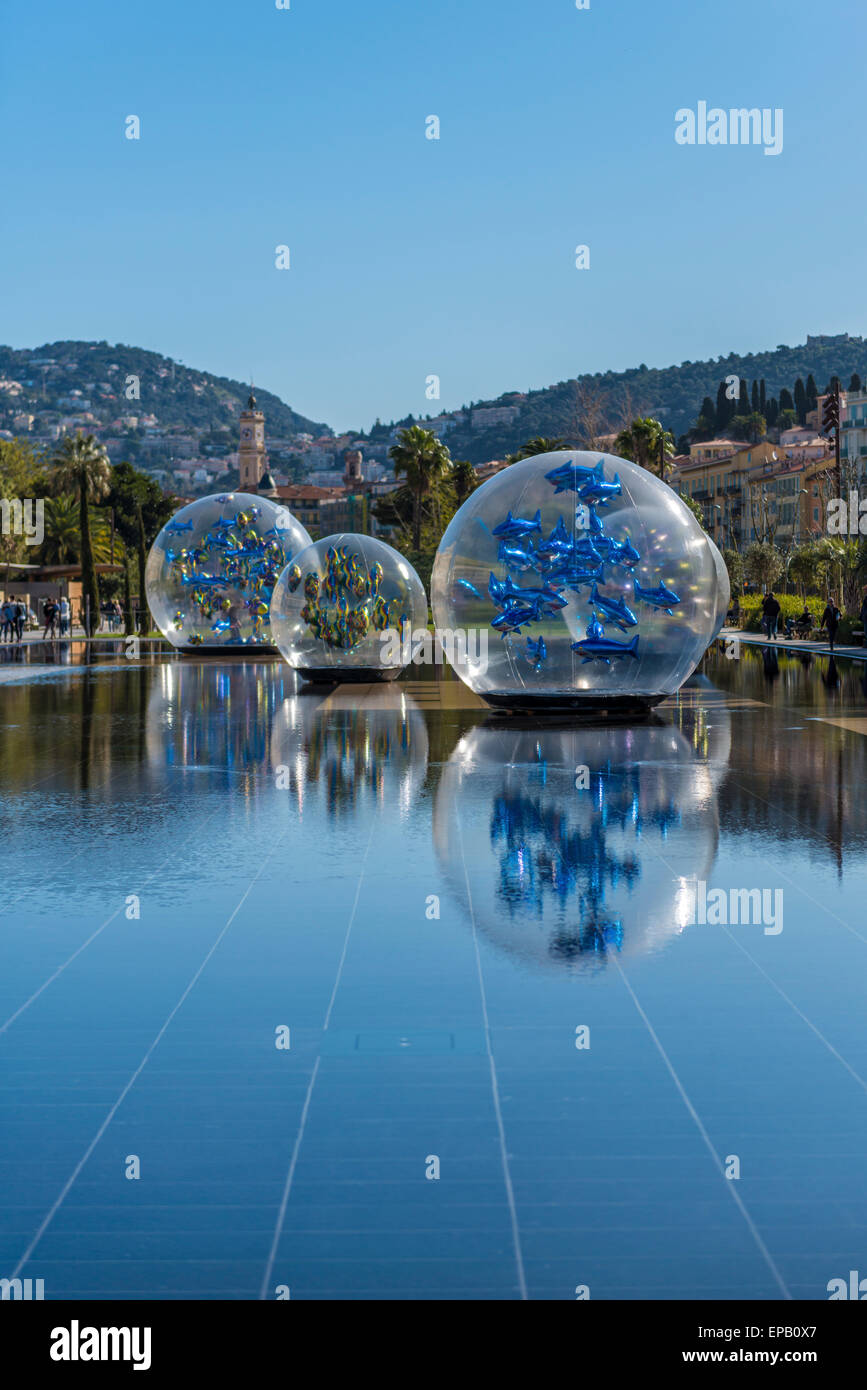 An art installation in a park in Nice featuring fish balloons in large clear globes reflected in the water on the ground Stock Photo