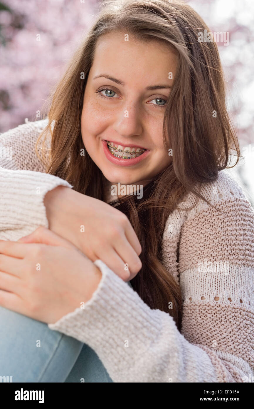 Girl with braces hugging knees in nature Stock Photo