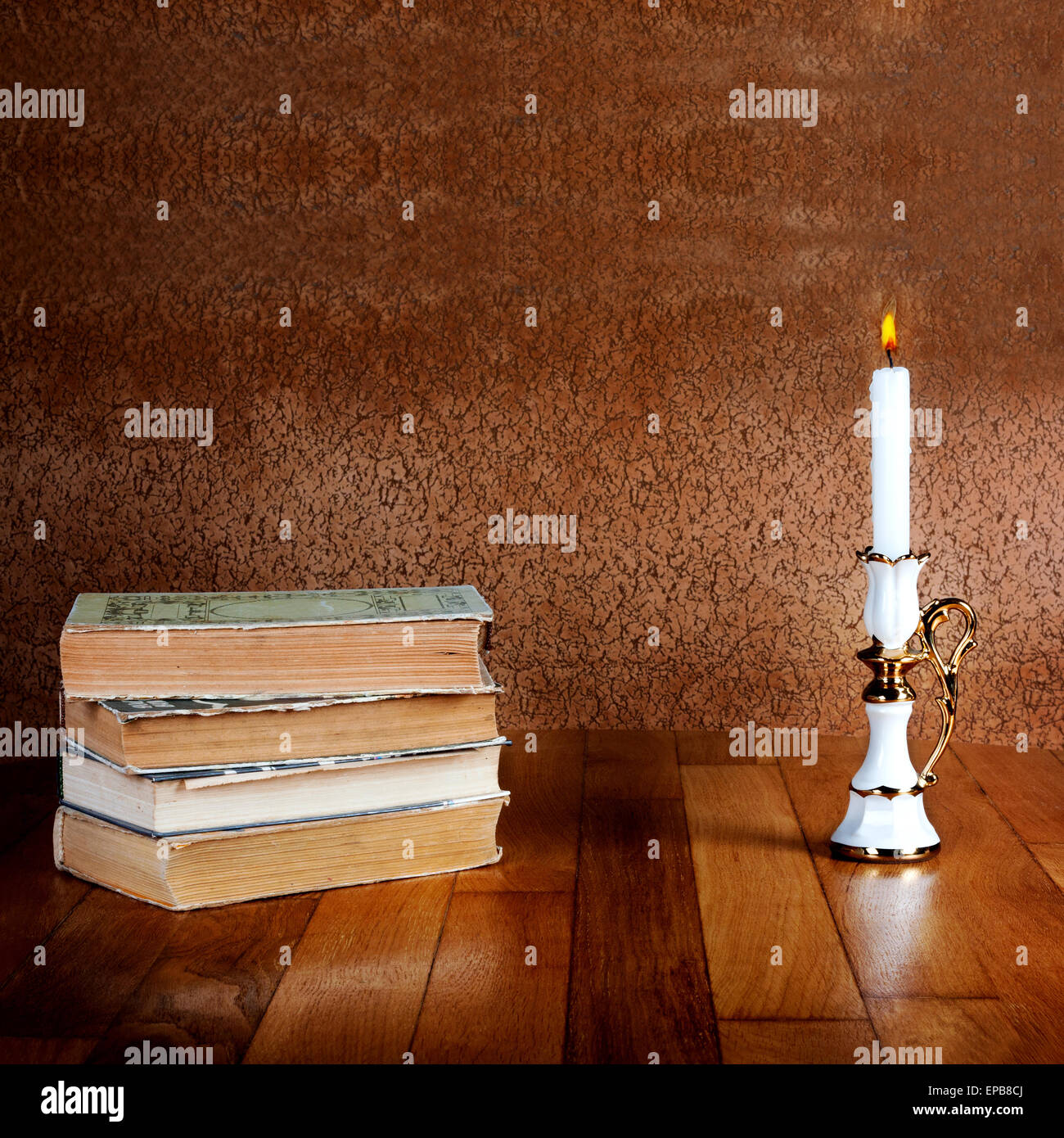 Old stack of books with candlestick and burning candle on the wooden table Stock Photo