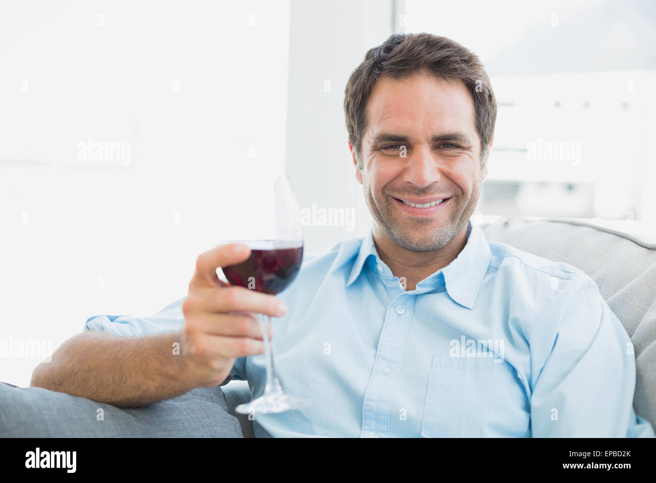 Happy man relaxing on sofa with glass of red wine Stock Photo - Alamy