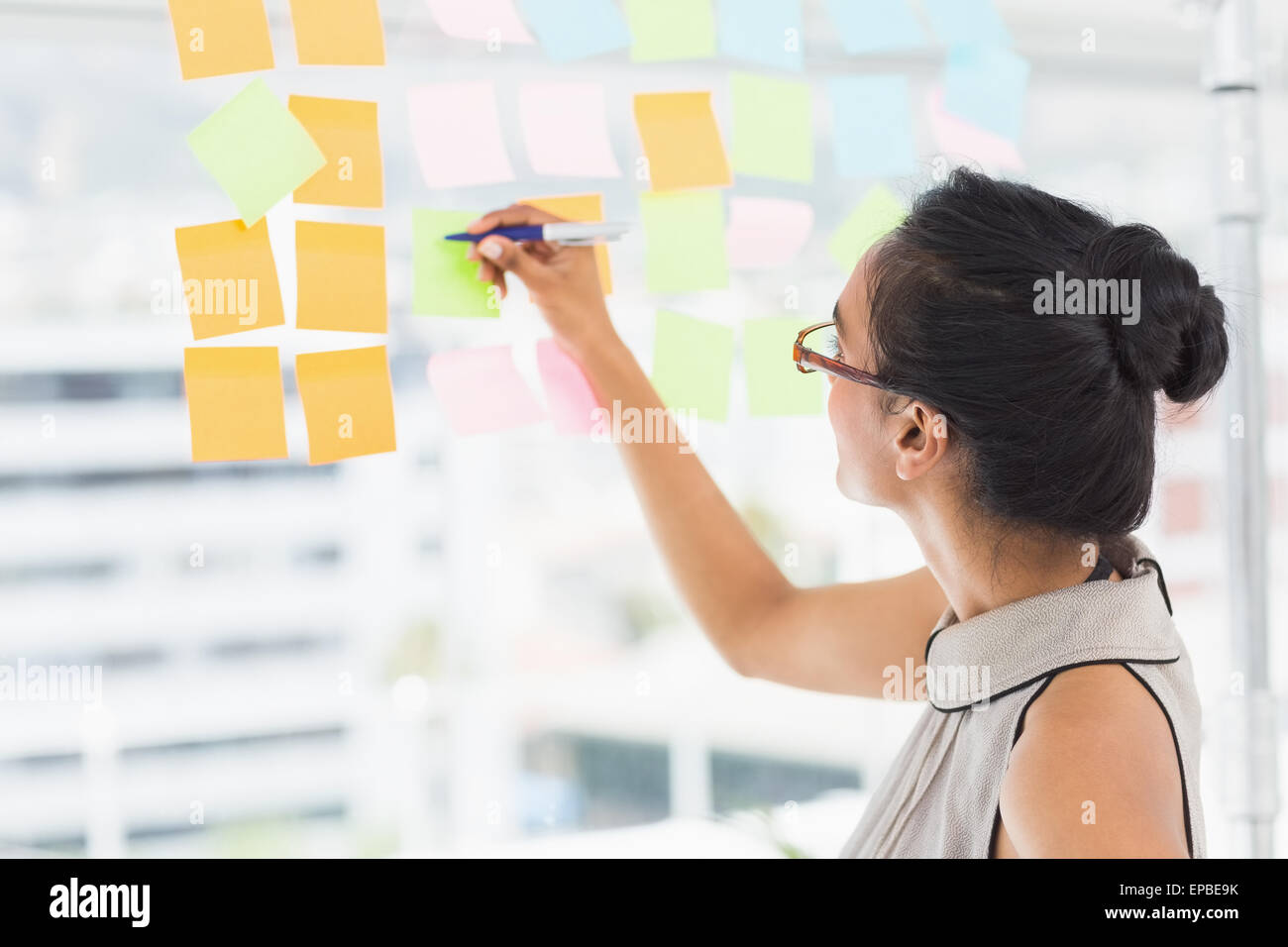 Smiling designer writing on sticky notes on window Stock Photo - Alamy