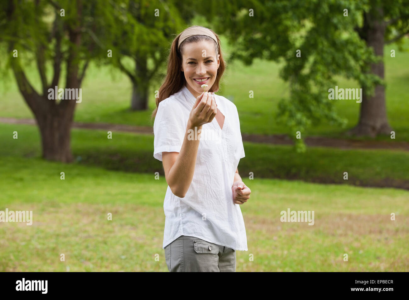 Smiling young woman holding a flower at park Stock Photo