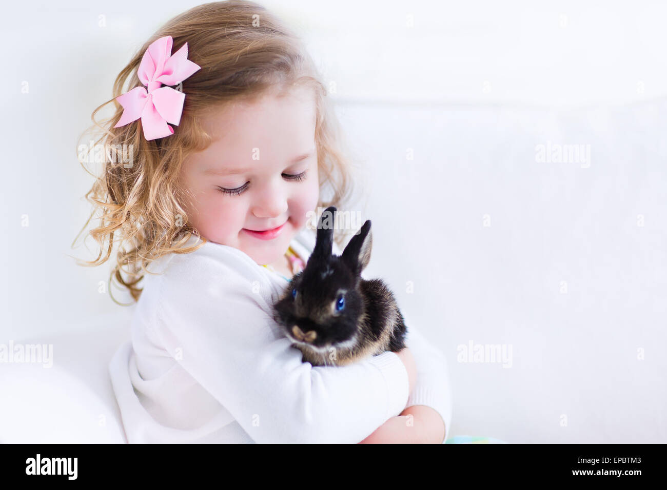 Happy laughing little girl playing with a baby rabbit, hugging her real