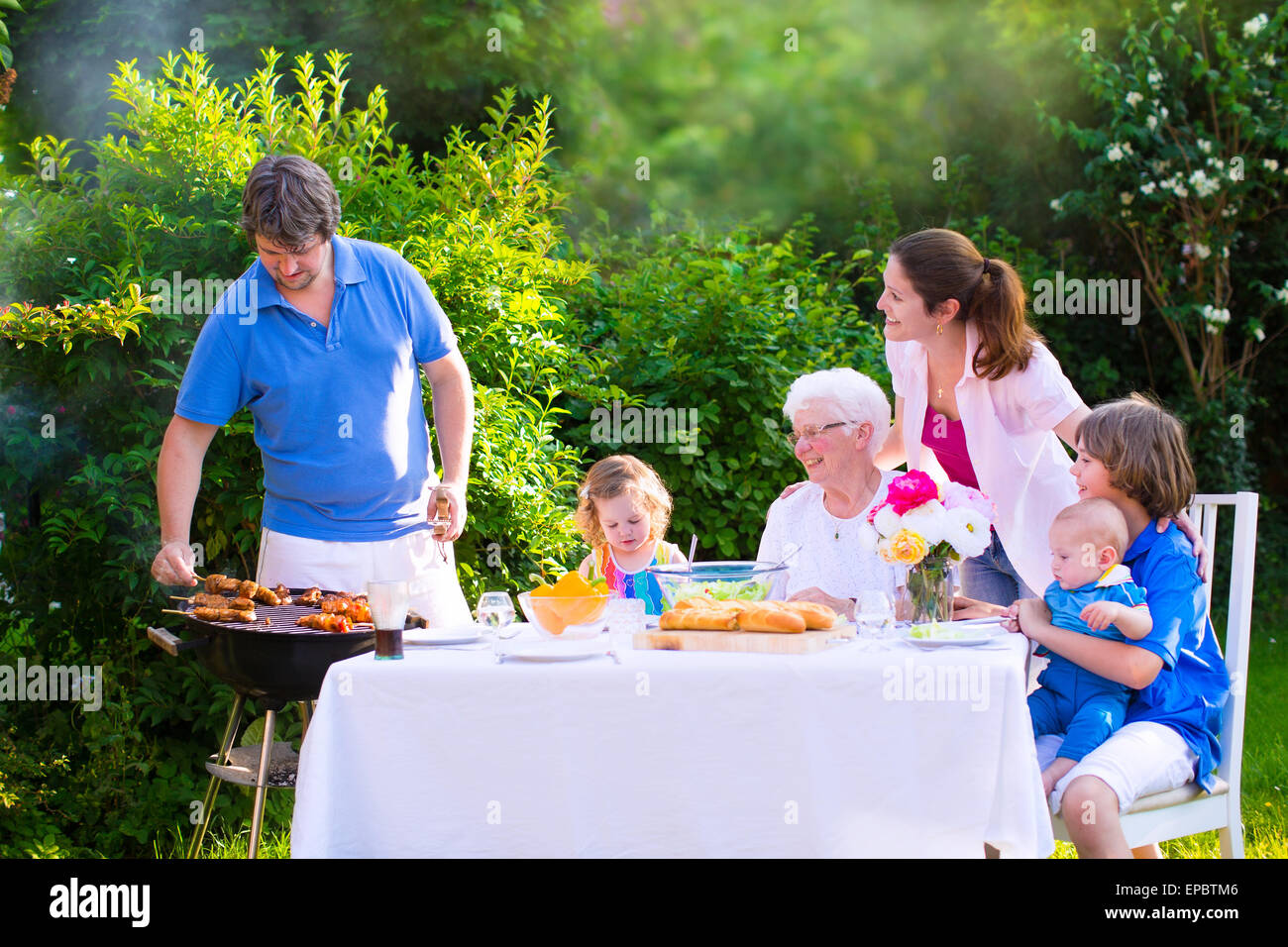 Grill barbecue backyard party. Happy big family enjoying BBQ lunch with grandmother eating grilled meat in the garden Stock Photo