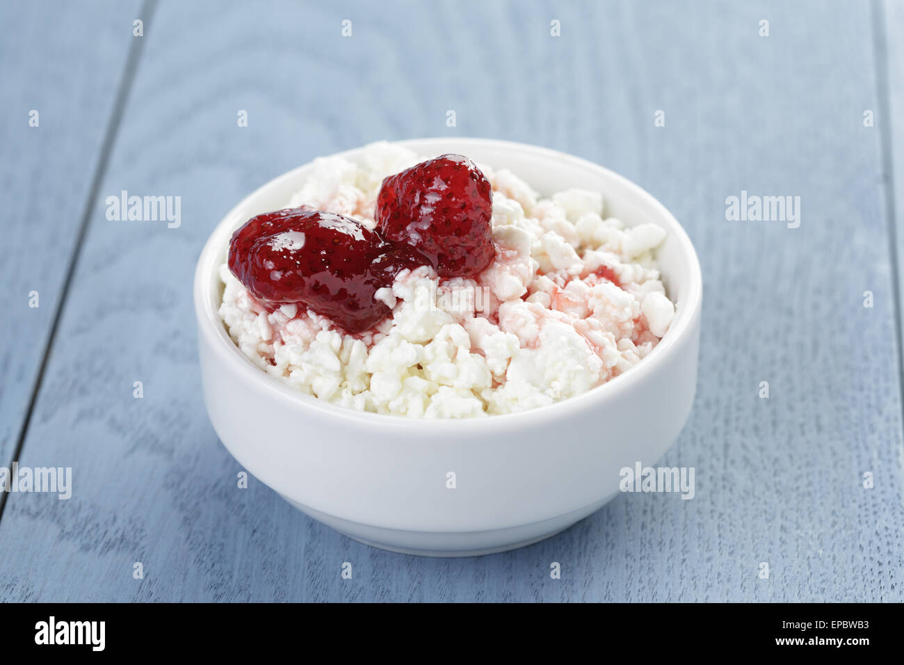 cottage cheese with strawberry jam in white bowl on blue wooden table