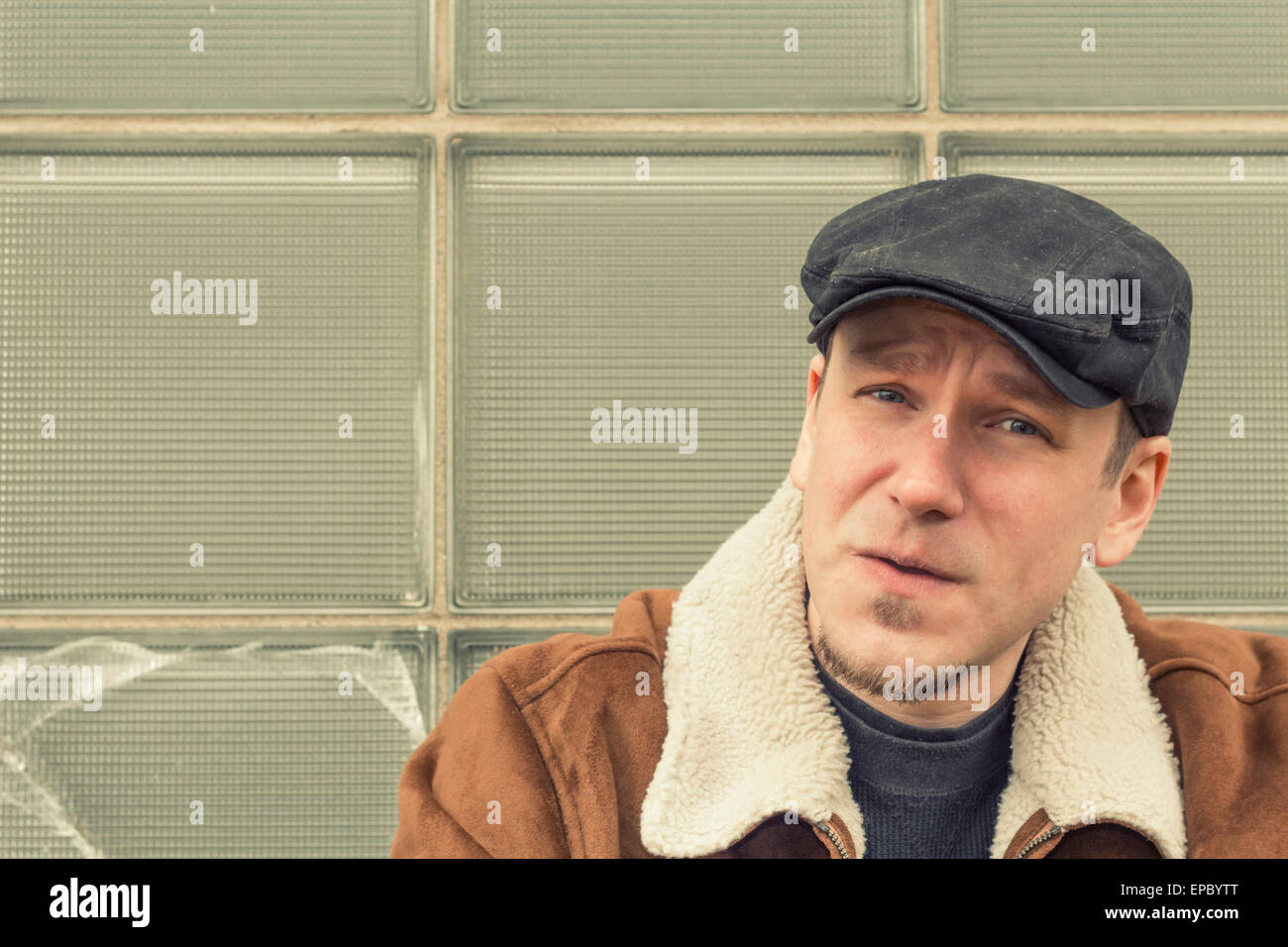 Cool guy in aviator jacket and newsie cap relaxes against a glass wall Stock Photo