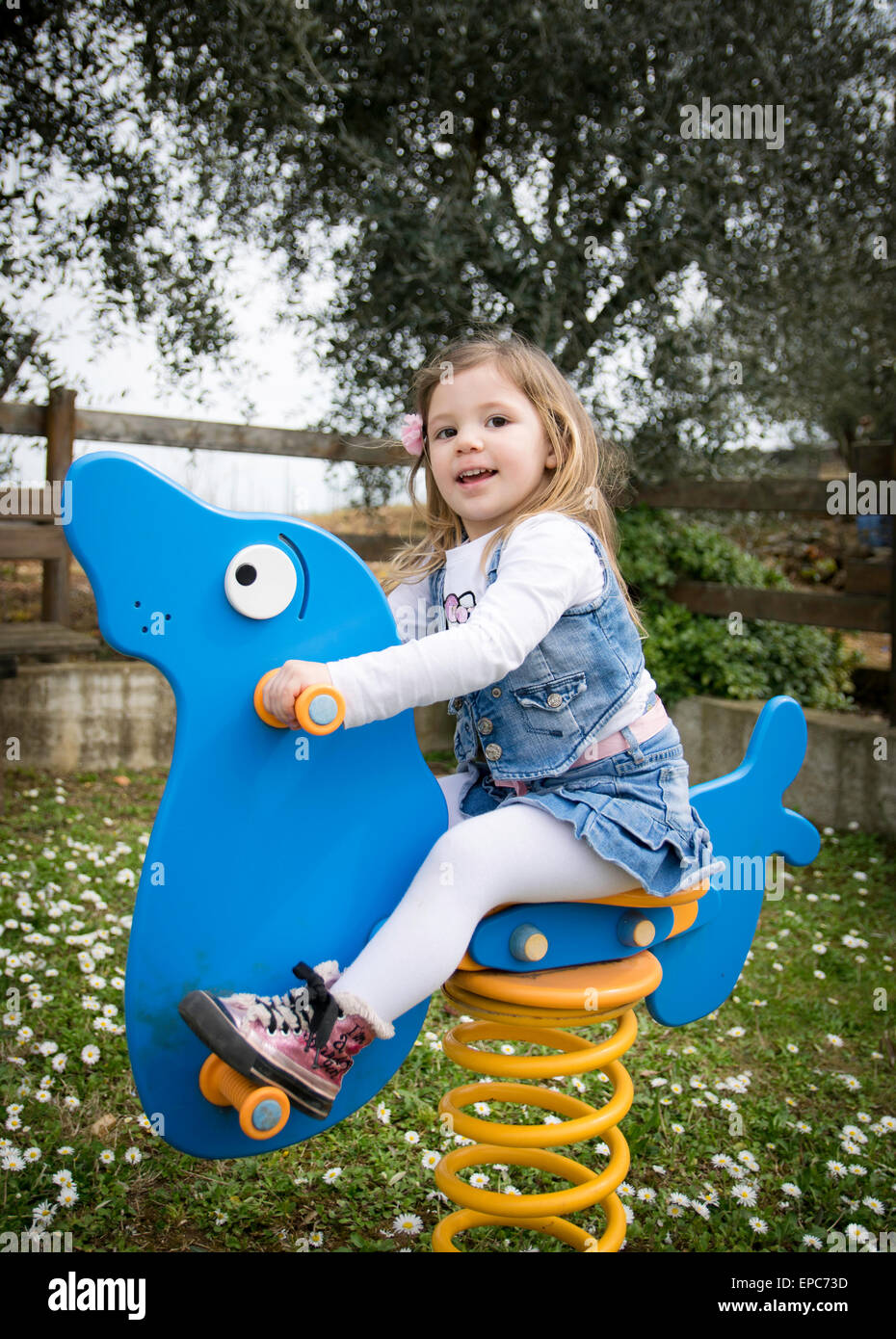 child plays on a blue spring seal in an outdoor playground Stock Photo