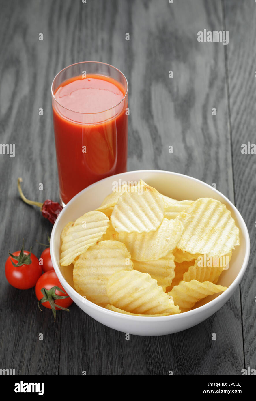 rippled organic chips in white bowl wit tomato juice on wooden table Stock Photo