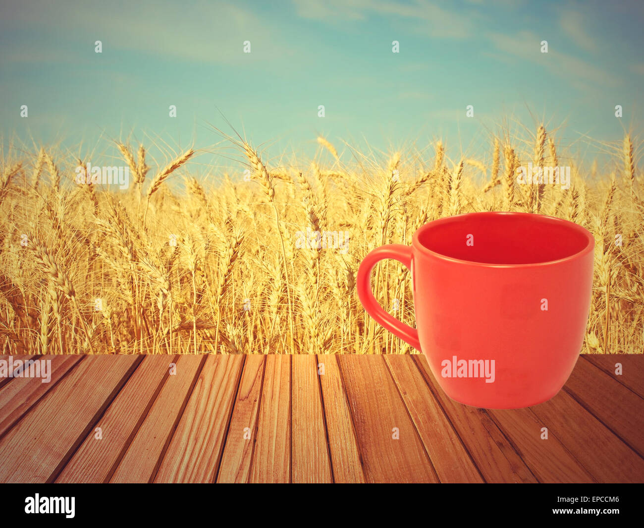 Red tea mug on wooden surface against of golden wheat ears and blue sky. Stock Photo