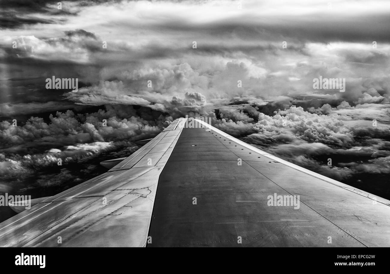 Wing of airplane flying in mid-air under and between clouds. Stock Photo
