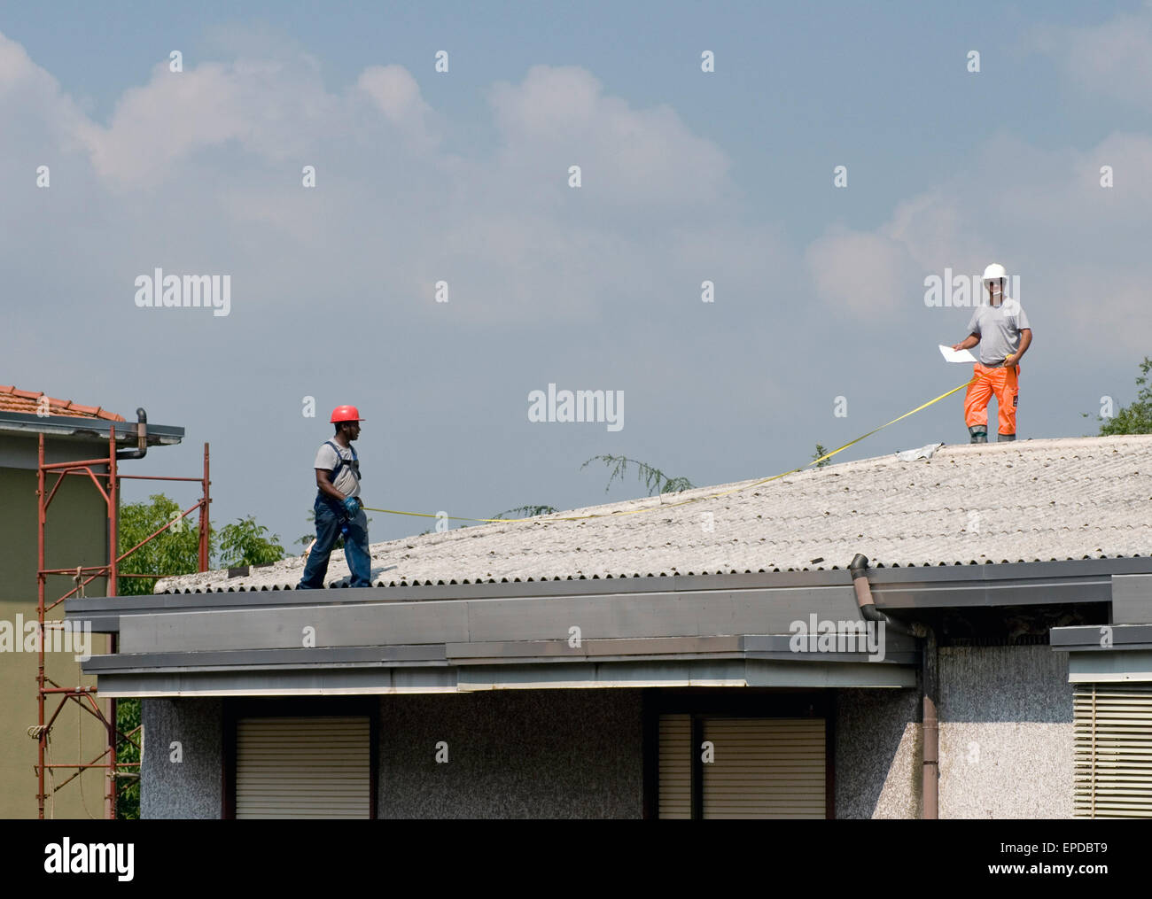 maintenance workers with measuring tape on corrugated asbestos eternit roof of a residential building, Italy Stock Photo