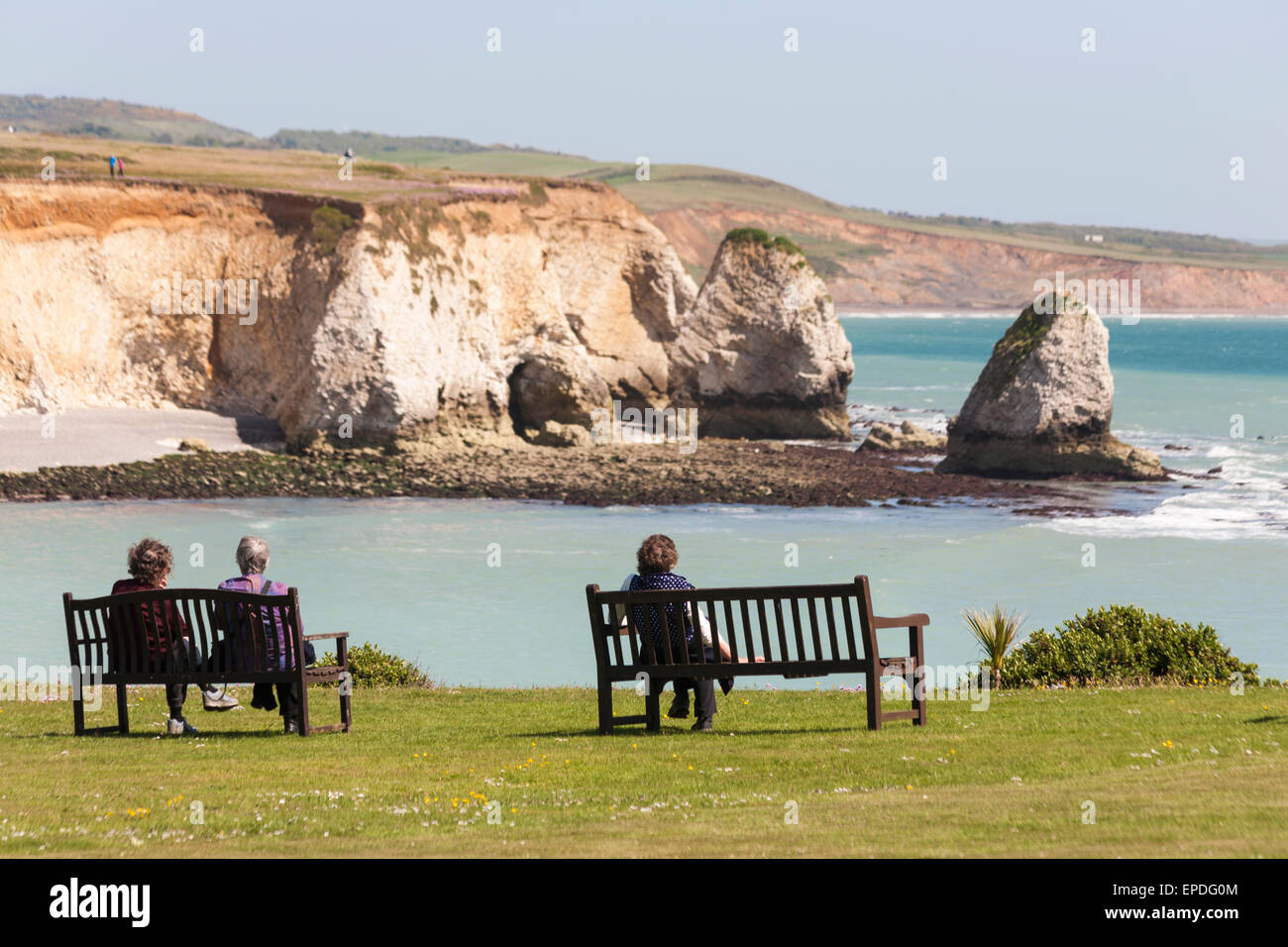 Women sitting on benches admiring the views at Freshwater Bay at Isle of Wight, Hampshire UK in May - seastacks sea stacks Stock Photo