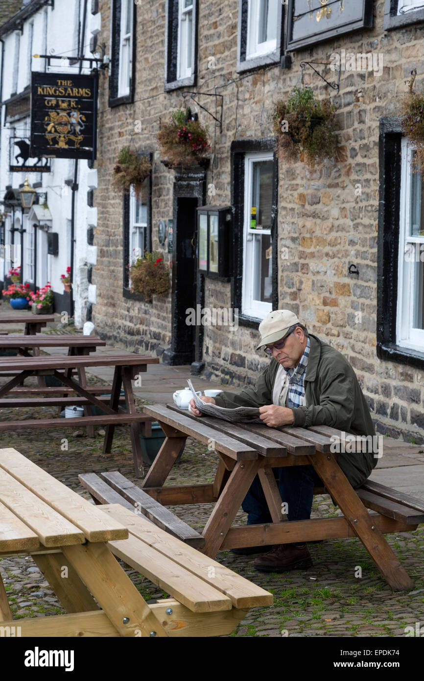 UK, England, Yorkshire, Reeth.  Man Reading the Newspaper outside the King's Arms Hotel. Stock Photo