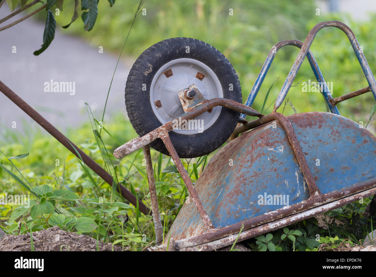 An old rusty blue wheelbarrow lying upside down in overgrown grass Stock Photo