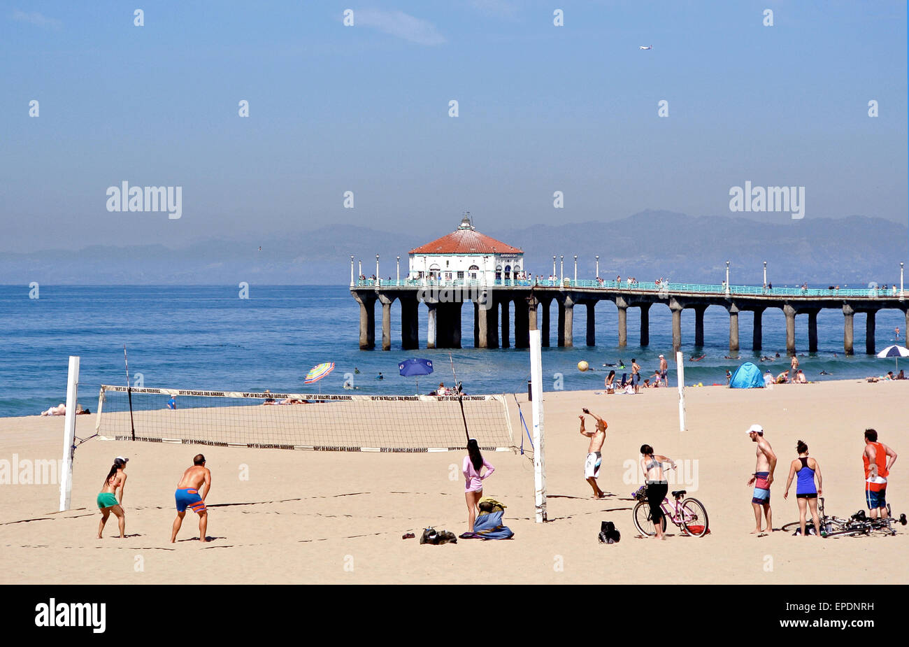 men and women play volleyball on Manhattan Beach California with the pier in the background Stock Photo