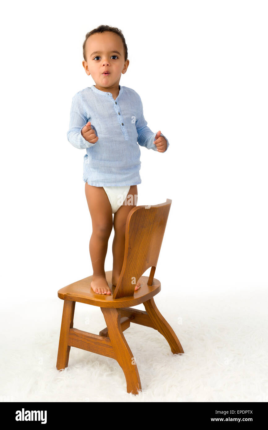 Cheerful little 18 month old toddler boy standing on a small wooden chair Stock Photo