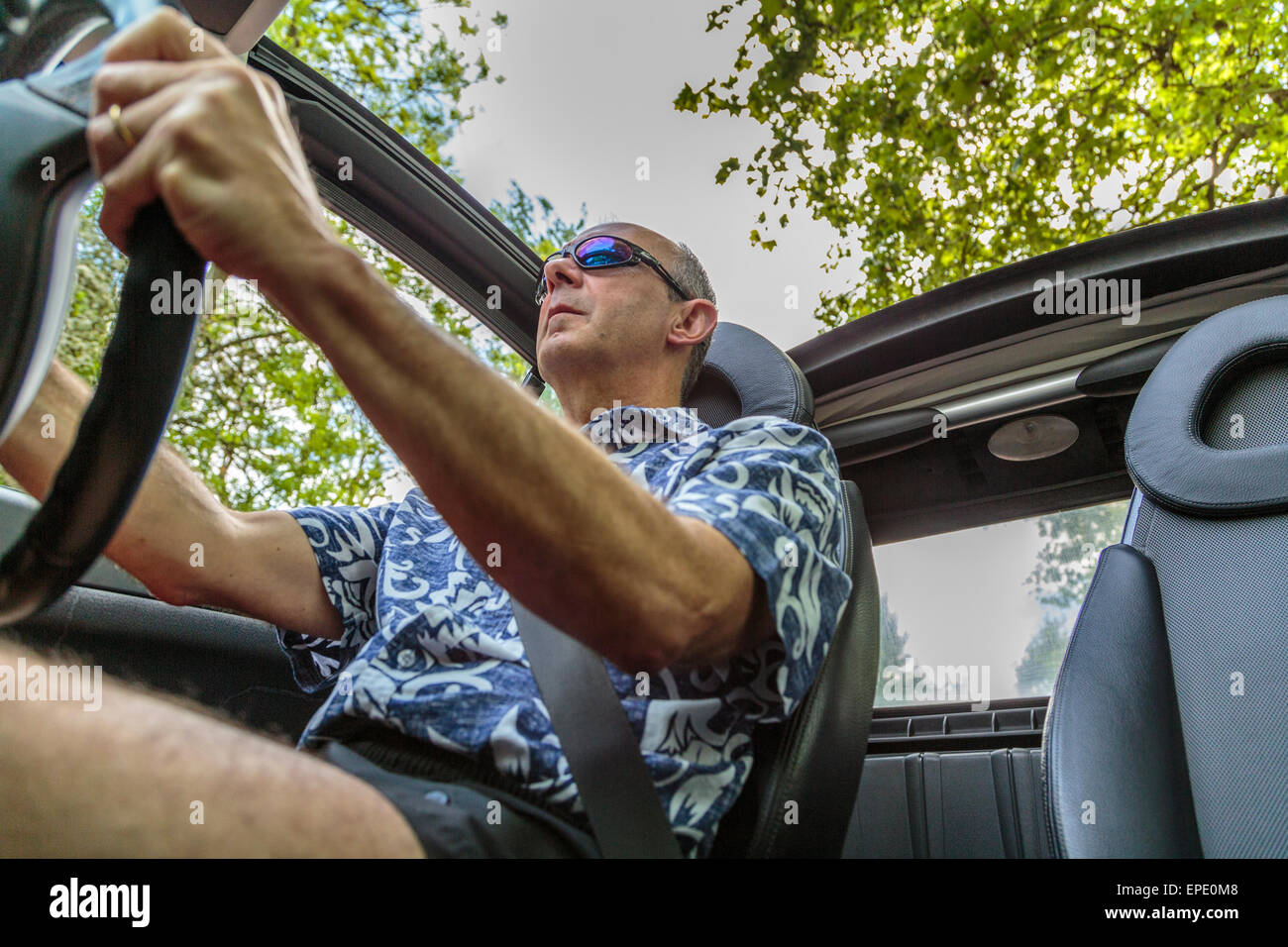 A middle aged man wearing sunglasses driving a Cabriolet car with the roof down on a summer day in Regents Park London England UK Stock Photo